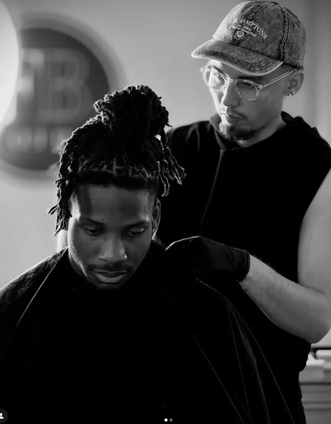 Barbier de Flux Barber installant la cape sur un client, devant le logo du salon